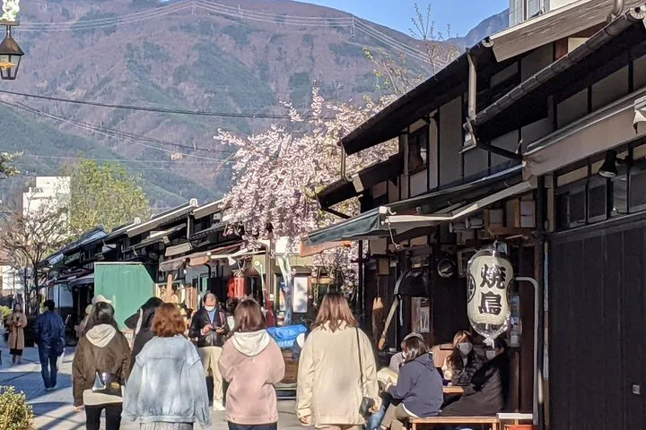 Personnes marchant dans une rue bordée de bâtiments traditionnels en bois et de cerisiers en fleurs