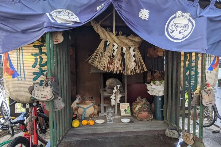 Petit sanctuaire avec des statues de grenouilles, une corde shimenawa et des lanternes en papier