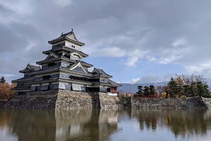 Außenansicht der Burg Matsumoto, umgeben von einem Burggraben unter bewölktem Himmel