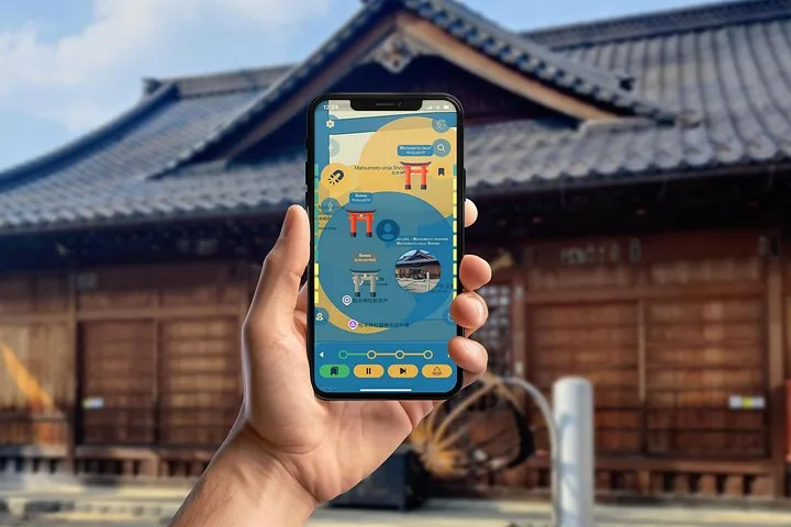 Main tenant un téléphone affichant une application avec carte devant un bâtiment traditionnel en bois